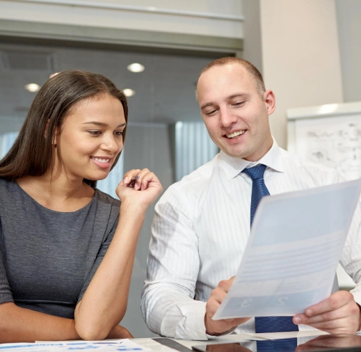 Dos colegas (un hombre y una mujer) sonriendo y colaborando mientras revisan un documento o contrato en una oficina.
